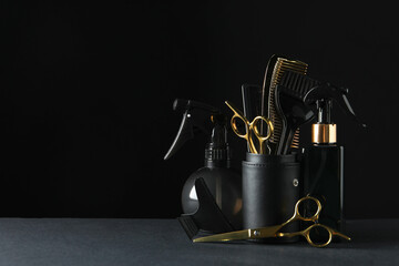 Different hairdresser tools on grey table against black background. Space for text