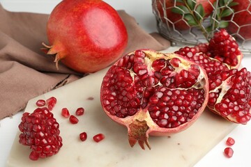 Piece of fresh pomegranate and seeds on white table, closeup