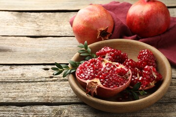 Fresh pomegranates and green leaves on wooden table, space for text