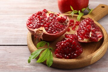 Fresh pomegranates and green leaves on wooden table, closeup. Space for text