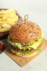 Burger with delicious patty and french fries on light table, closeup