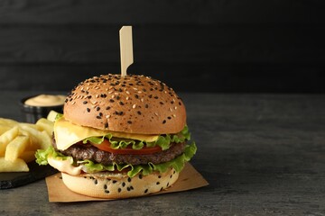 Burger with delicious patty and french fries on gray table against dark background, space for text