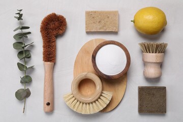 Cleaning brushes, baking soda, lemon, soap bar and eucalyptus leaves on white table, flat lay