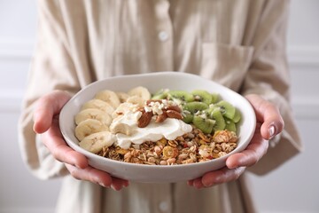 Woman holding bowl of tasty granola indoors, closeup