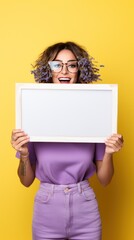 Photo of A woman holding up an empty frame with space for text on teal background, excited expression, wearing sunglasses and yellow dress