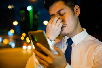 Tired businessman in suit rubbing eyes after using smartphone at night. Frustration due to eye...