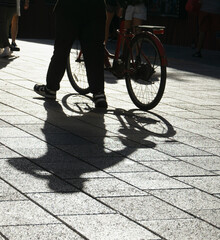 Silhouette of a person and bicycle casting long shadows on a tiled street in Playa del Carmen Mexico, with indistinct bystanders