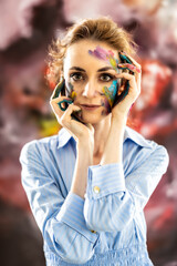Woman Painter of abstract paintings painted with paints on her face, posing in front of her painting - 785284056