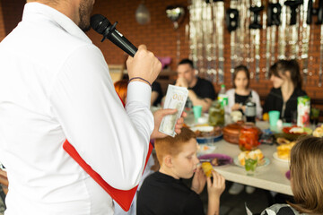 A man in a white shirt holds money speaks into the microphone in a restaurant