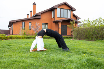 Young woman doing yoga in front of her new house on the grass. Young woman doing bridge exercise.