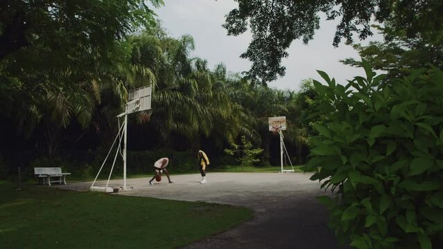 Extreme long shot of two male athletes playing basketball on court in local park