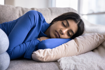 Calm sleepy young Indian woman lying on side on soft home couch with arms under head, sleeping at daytime for recreation, enjoying leisure, silence, calmness, comfort - 785289419