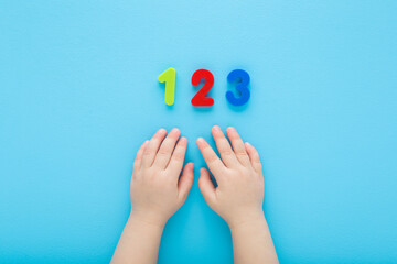 Baby boy hands and colorful 123 numbers on light blue table background. Pastel color. Time to learning. Closeup. Point of view shot. Top down view.