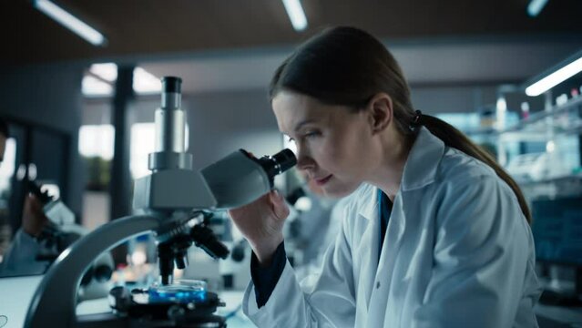 Portrait of a Beautiful Caucasian Student Working on a Research Project in College. Medical Research Scientist Looking at Biological Samples Under a Microscope in an Applied Science Laboratory - Powered by Adobe