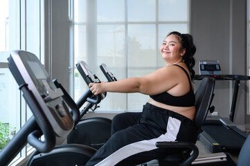 Asian overweight women exercising on the exercise bike in indoor fitness club. Healthy and Fitness...