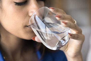 Peaceful thirsty young Indian woman drinking clear water with closed eyes, holding glass, caring for healthy lifestyle, hydration, aqua balance, promoting skincare. Cropped close up shot of face - 785296462