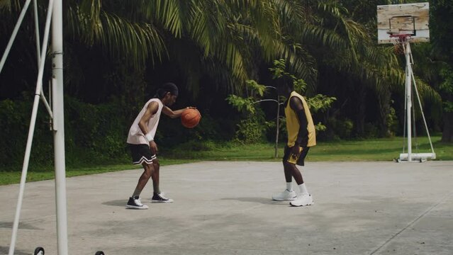 Wide shot of African American sportsman passing ball to another player during streetball training on outdoor court