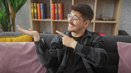 Smiling hispanic man with glasses and moustache presenting invisible product in a cozy home...