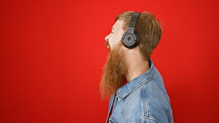 Young redhead man listening to music doing thumbs up gesture over isolated red background