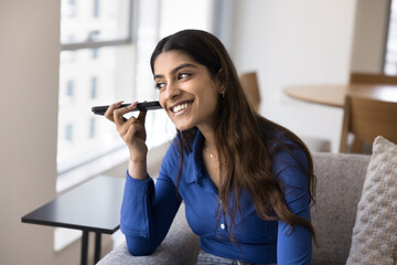 Happy Indian gadget user girl listening to audio message on mobile phone, smiling, laughing, using smartphone at home, enjoying smart AI technologies, Internet connection - 785298425