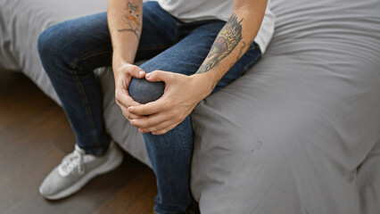 Aching hands of an adult man suffering from a knee injury, touching it painfully on a bed in a...