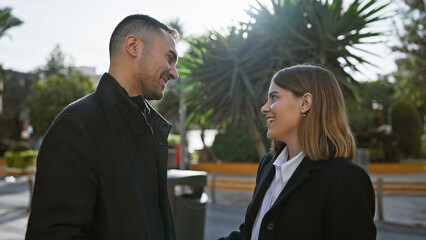 A loving couple stands together outdoors on a sunny city street, with a backdrop of palm trees and urban architecture.