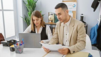 A professional man and woman review documents together in a bright modern office interior.