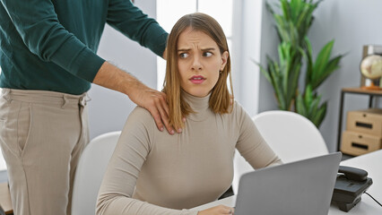 Woman feels uncomfortable as man places hand on her shoulder in a modern office setting.