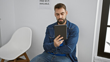 Young hispanic man sitting on chair using touchpad at waiting room