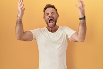 Middle age man with beard standing over yellow background celebrating mad and crazy for success...