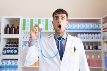 Young hispanic man wearing doctor uniform and stethoscope scared and amazed with open mouth for surprise, disbelief face