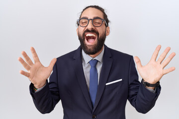 Hispanic man with beard wearing suit and tie celebrating mad and crazy for success with arms raised...