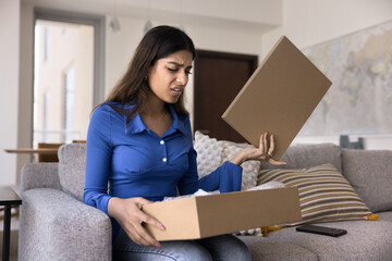 Upset concerned young Indian customer woman opening logistic cardboard box, receiving wrong parcel, purchase, finding damage, mistake of transportation service, looking inside container - 785303873