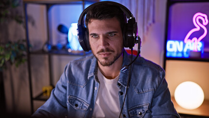 Handsome bearded man wearing headphones in a dark gaming room with vibrant neon lights.