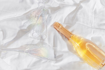 Romance concept, lifestyle photo minimal style, two bright glasses with rainbow shadow, white wine bottle on white bedclothes at home, natural light, top view close up, star filter, copyspace