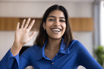 Cheerful beautiful young Indian blogger girl waving hand hello at camera, saying hi, greeting blog audience, talking on online video conference call, starting broadcast on Internet - 785304816