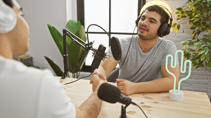 Two men engaging in a podcast conversation in a bright, modern studio setup with professional audio...