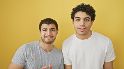 Two hispanic men standing closely, expressing friendship against a vibrant yellow background