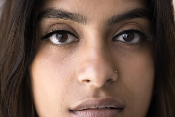Face close up of young Indian woman with smooth clean facial skin posing for cropped portrait. Beautiful female Indian beauty care model with nose stud, long eyelashes looking at camera