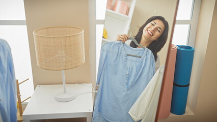 Smiling middle-aged hispanic woman trying on blue shirt in bright dressing room