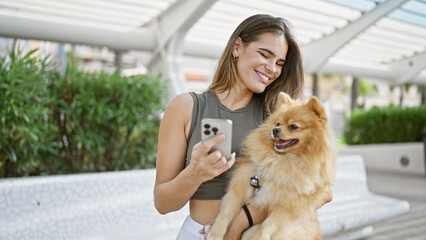 Young, confident hispanic woman joyfully smiling, hugging her beautiful pet dog, while cheerfully...