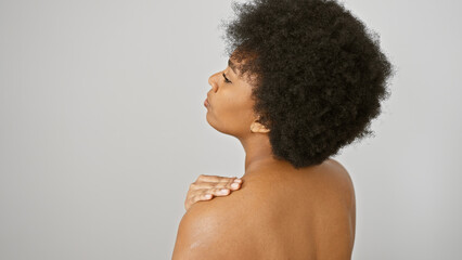 A beautiful african woman with curly hair applies cream on her shoulder against a white background.