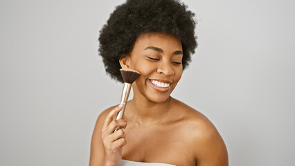 A joyful african woman applies makeup with a brush against a white background, embodying beauty and...