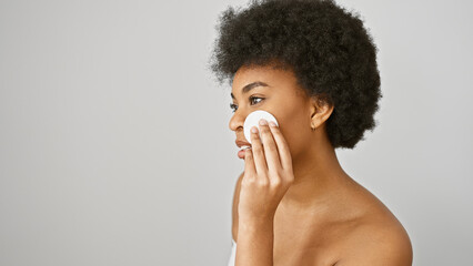 African american woman with curly hair applying a cotton pad to her face against a white background.
