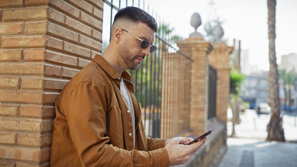 Handsome hispanic man with beard using smartphone on sunny urban street