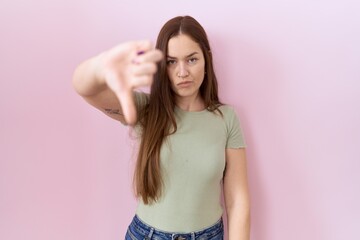 Beautiful brunette woman standing over pink background looking unhappy and angry showing rejection...