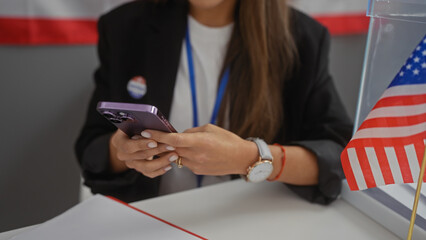 A young hispanic woman uses a smartphone indoors with an american flag in the foreground.