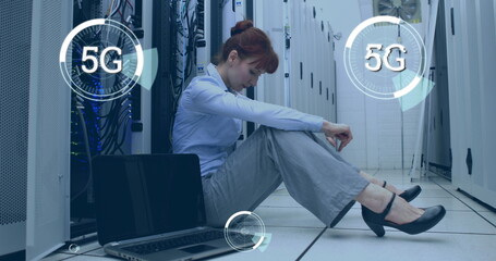 Digital composite of a Caucasian woman sitting beside a laptop in a corridor of server towers while 