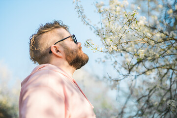 Portrait of curly millennial man inhales the fragrance of spring flowers of blooming jasmine or...