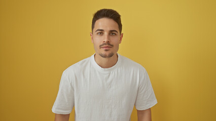 Portrait of a handsome young hispanic man with a beard wearing a white shirt against a yellow...